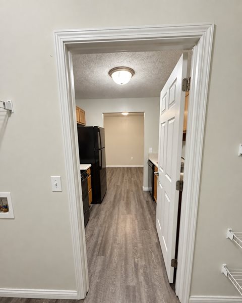 A hallway with a black refrigerator and wooden cabinets.