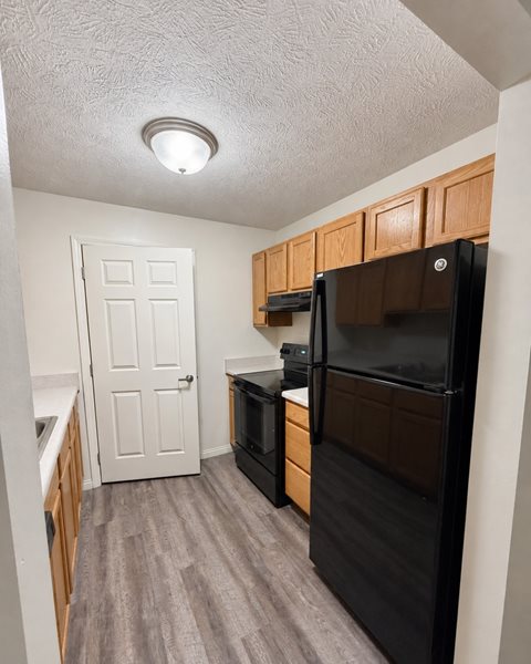 A black refrigerator in a kitchen with wooden cabinets.