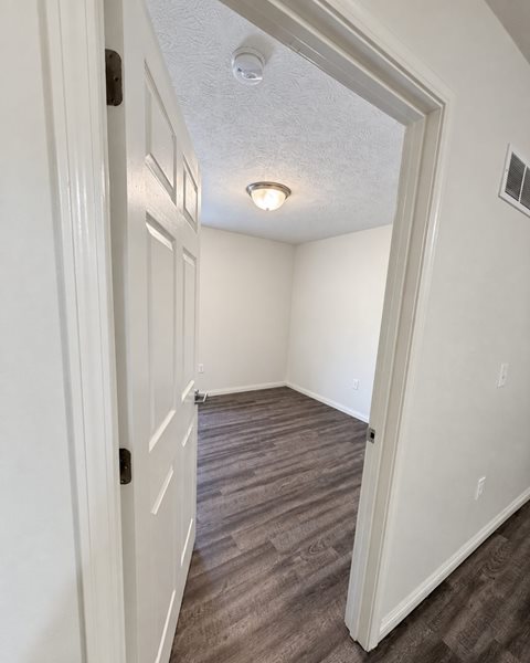 A white door is open to a room with wood flooring.