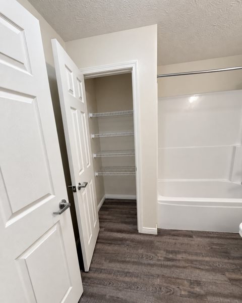 A white door is open to a small pantry with a bathtub in the background.