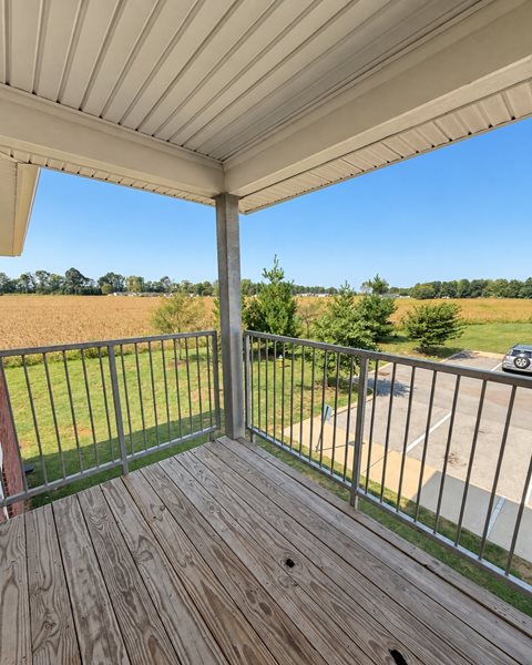 A wooden deck with a metal railing and a view of a parking lot and trees.