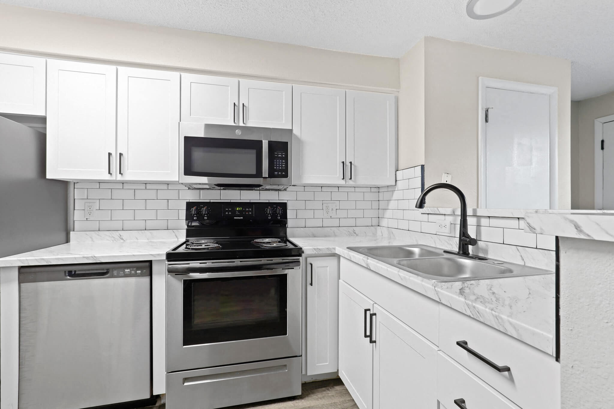 Fully updated kitchen with white shaker cabinets, subway tile backsplash, black fixtures, and stainless steel appliances at 1443 Elizabeth in Denver, CO