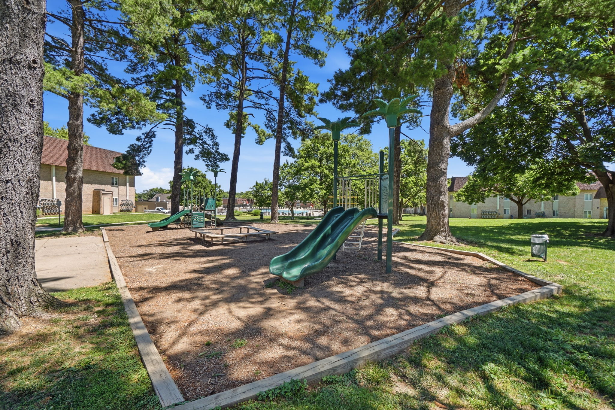 A playground with a green slide and a wooden fence.