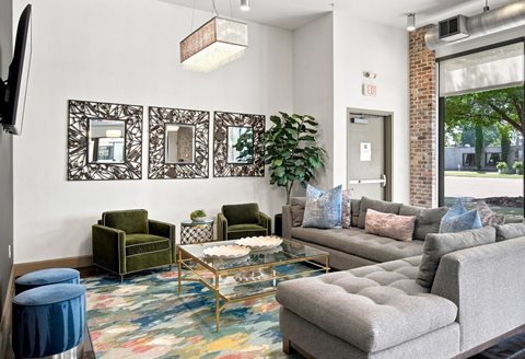 A living room with a grey couch, a green chair, and a glass coffee table.