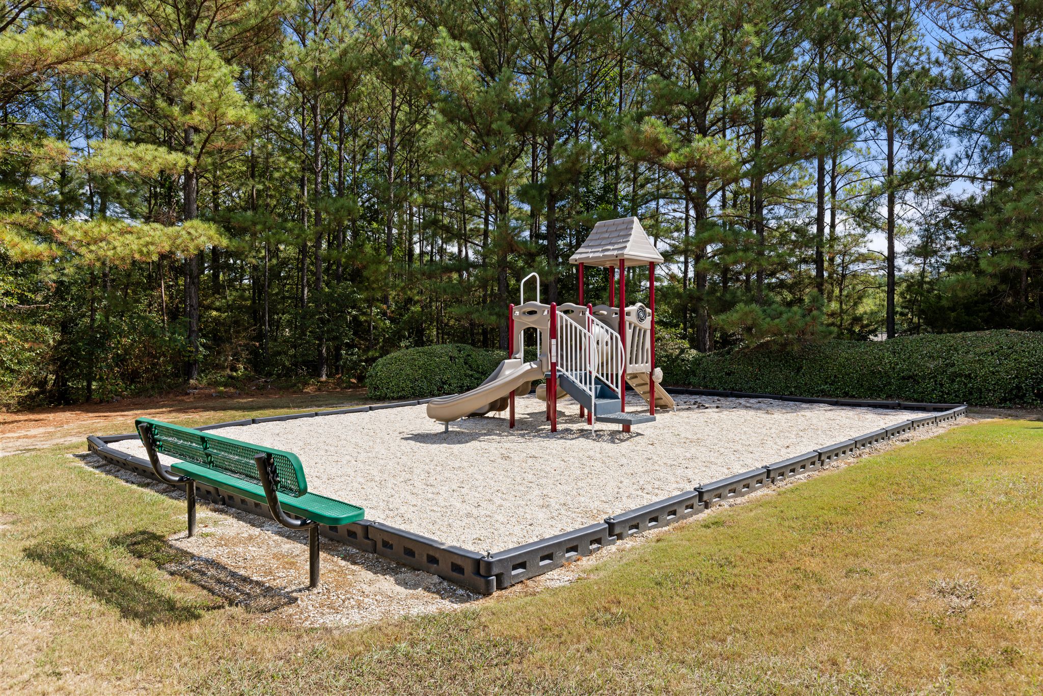 A playground with a green bench and a red slide.
