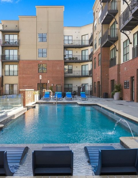 A pool surrounded by a brick building and lounge chairs.