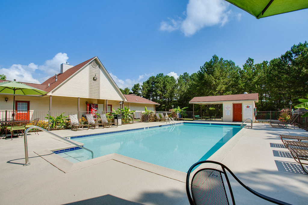 A pool area with a chair and a house in the background.
