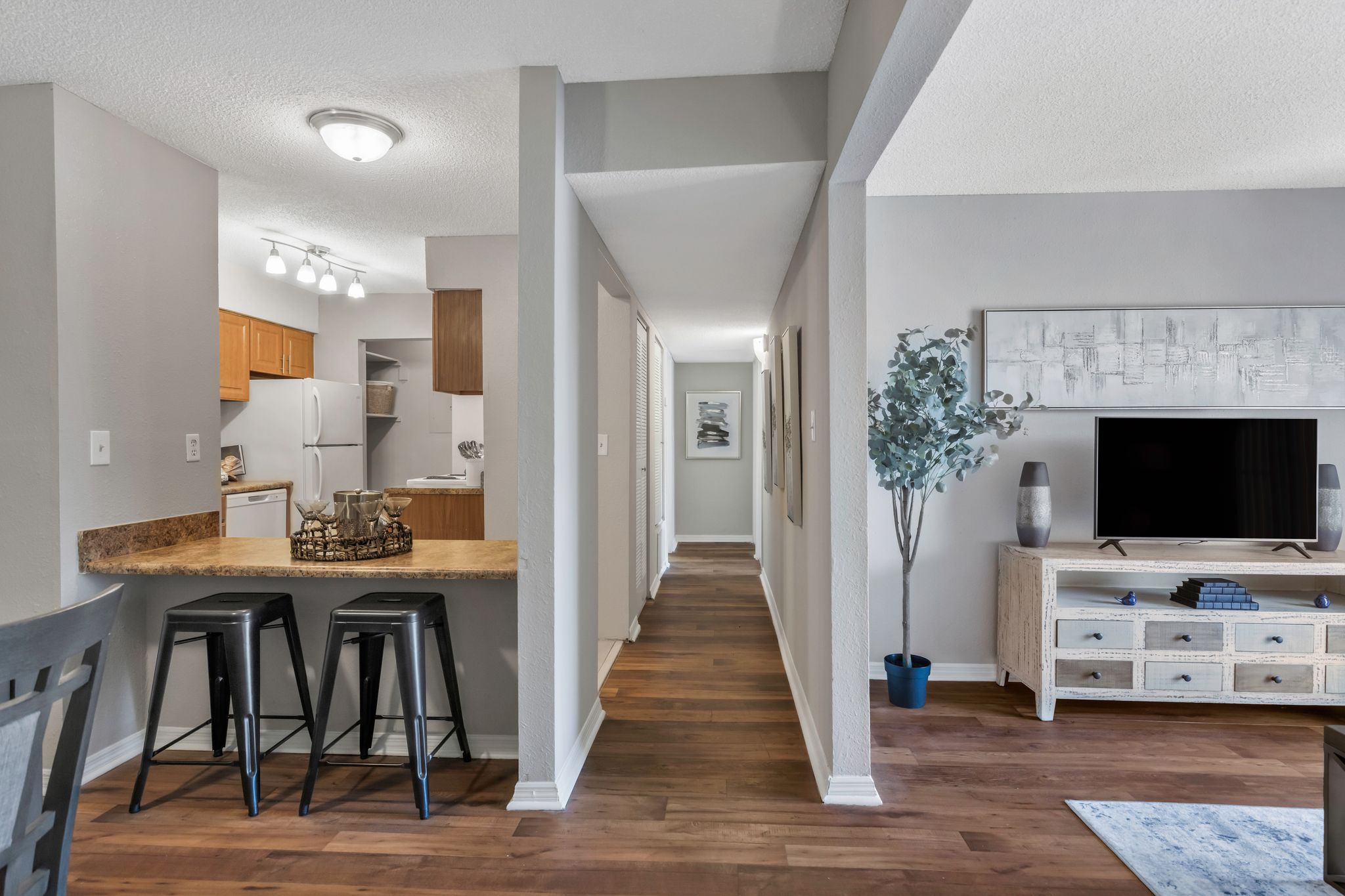 A long hallway with a kitchen area on the left and a living room area on the right.