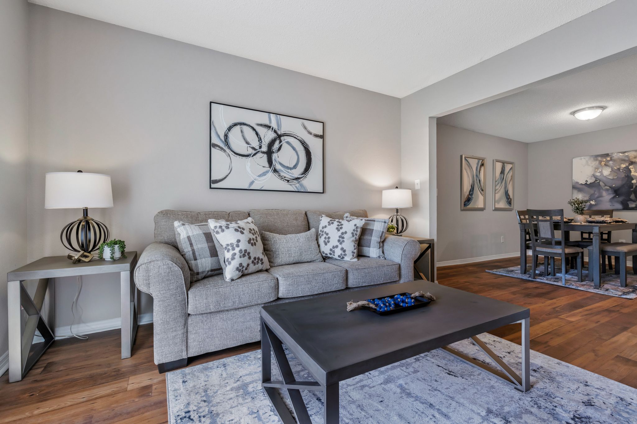 A modern living room with a grey couch, a coffee table, and a dining table set in the background.