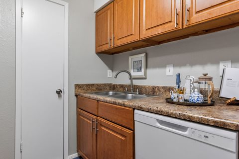 A kitchen with a white door, brown cabinets, and a white dishwasher.