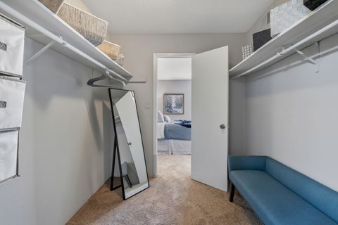 A room with a mirror, a bench, and a bed in the background.