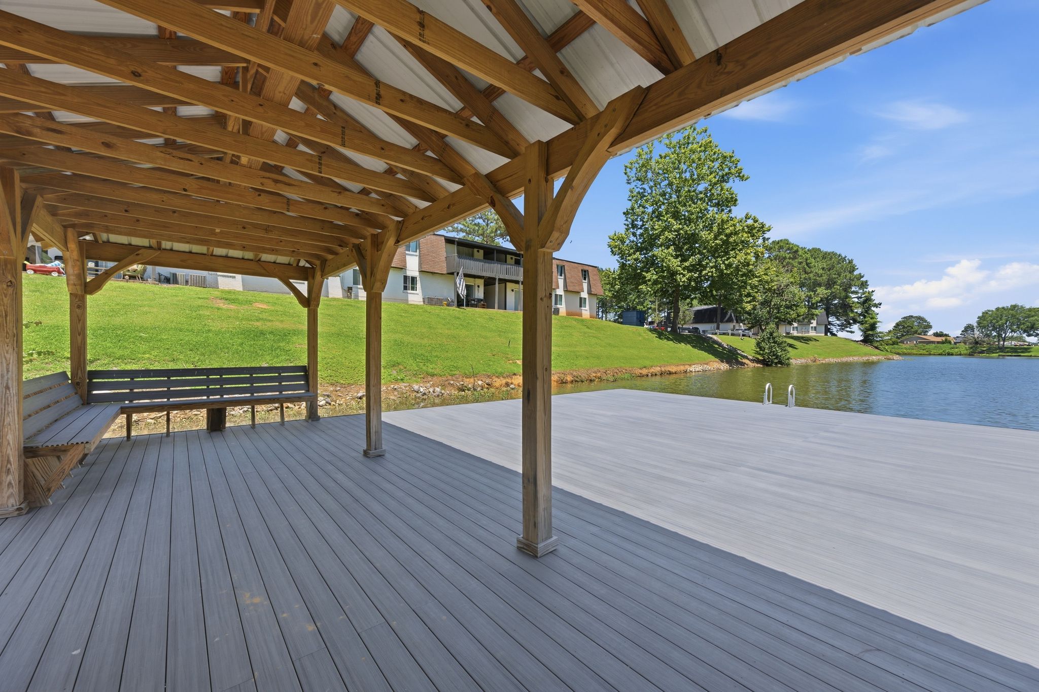 A wooden pavilion with a bench is situated on a wooden deck overlooking a lake.
