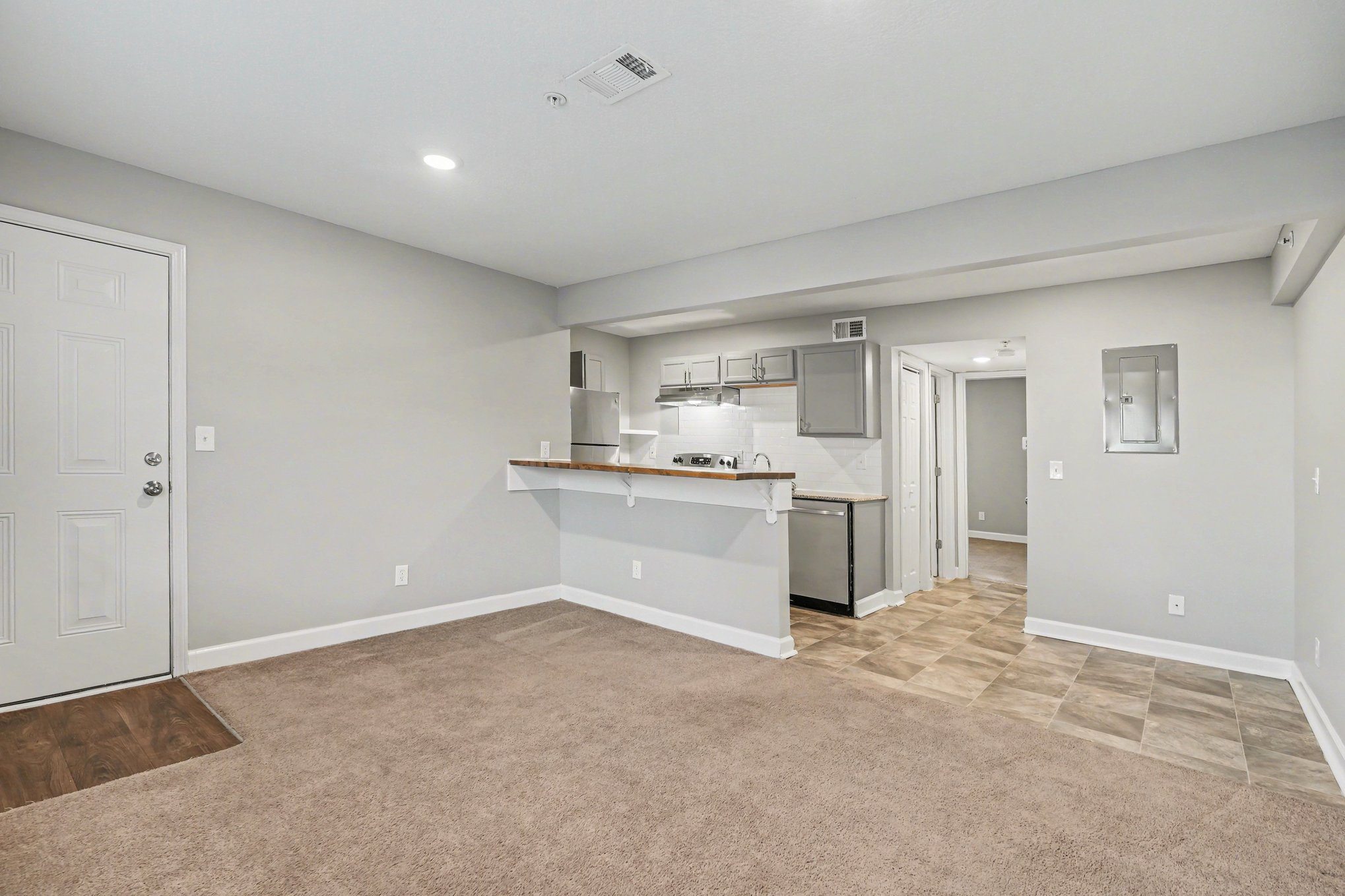 A spacious room with a kitchenette and a door leading to another room.