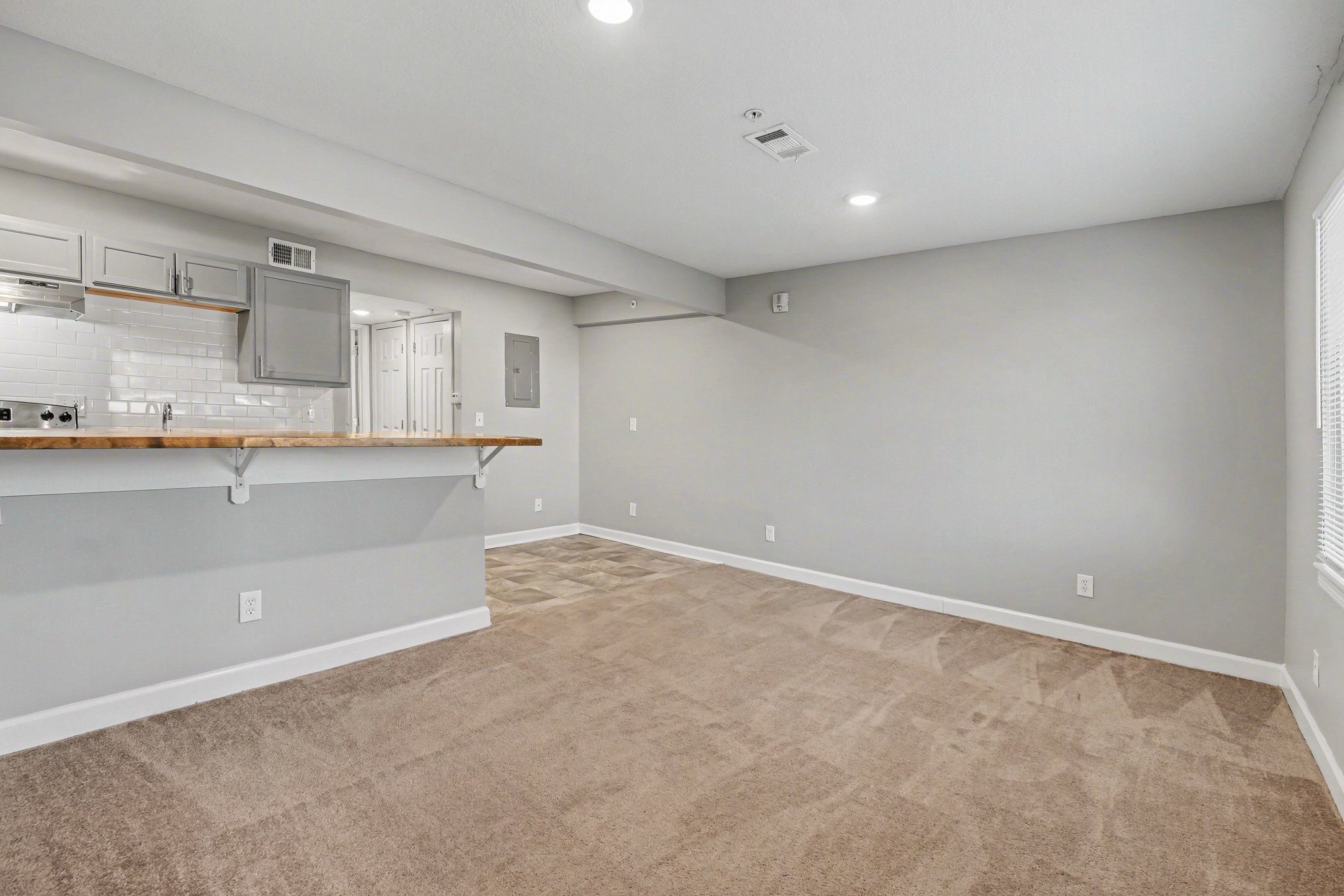 A spacious room with a kitchenette and beige carpeting.