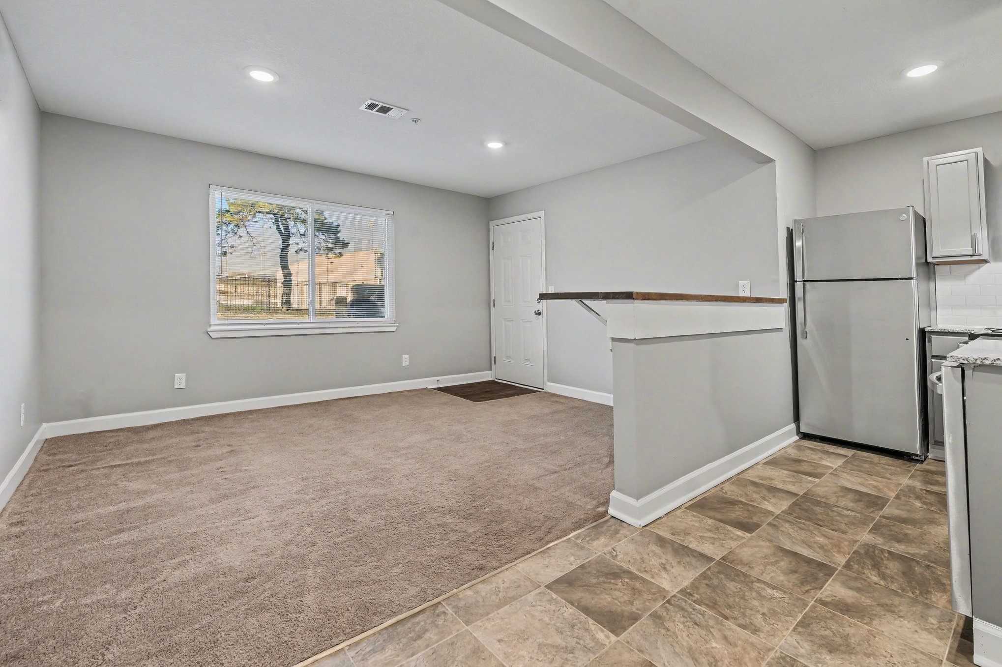 A spacious kitchen with a refrigerator and a painting of a tree on the wall.