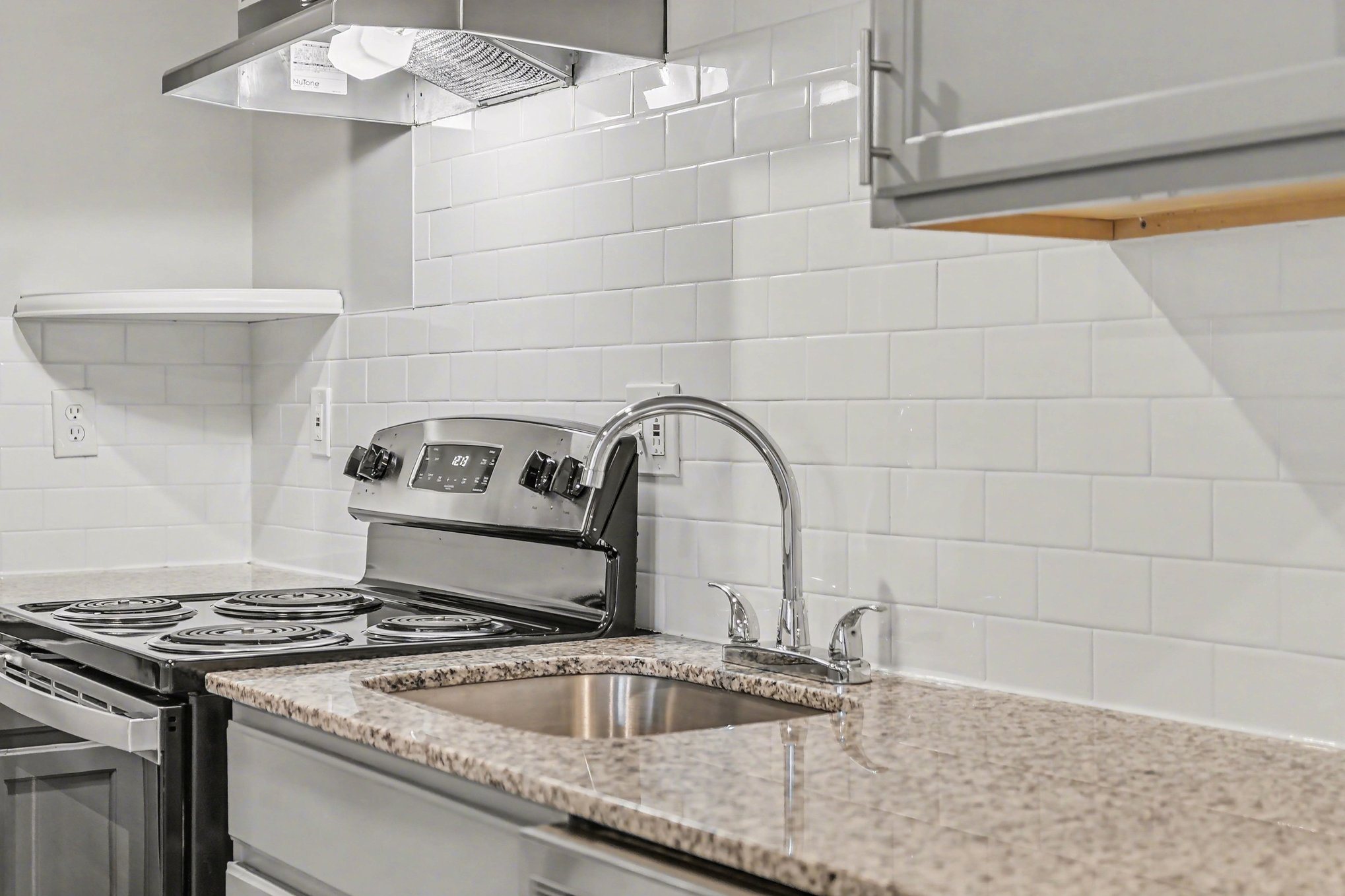 A kitchen with a stove, sink, and a white tile backsplash.