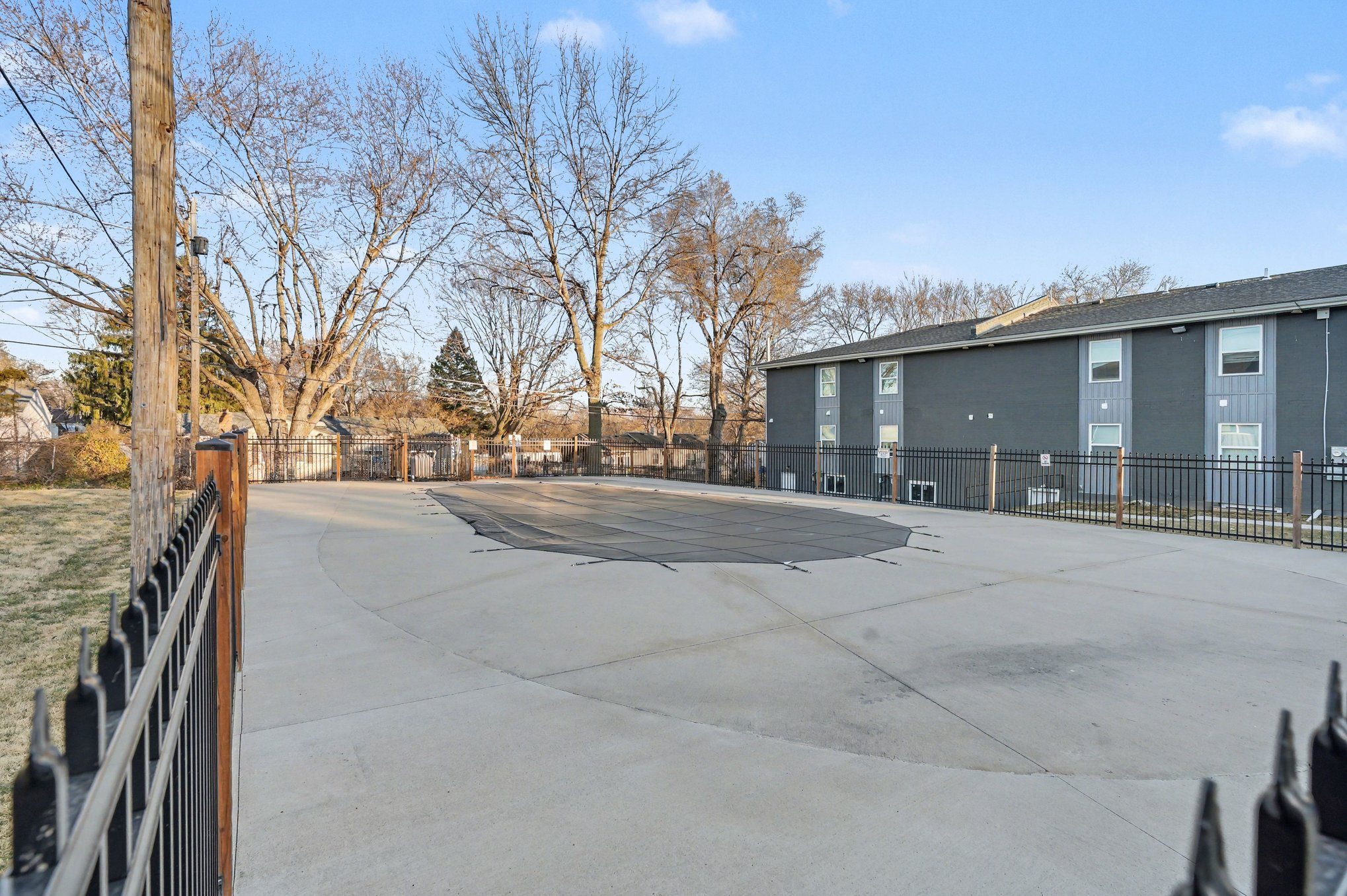 A parking lot with a building in the background and a fence in the foreground.