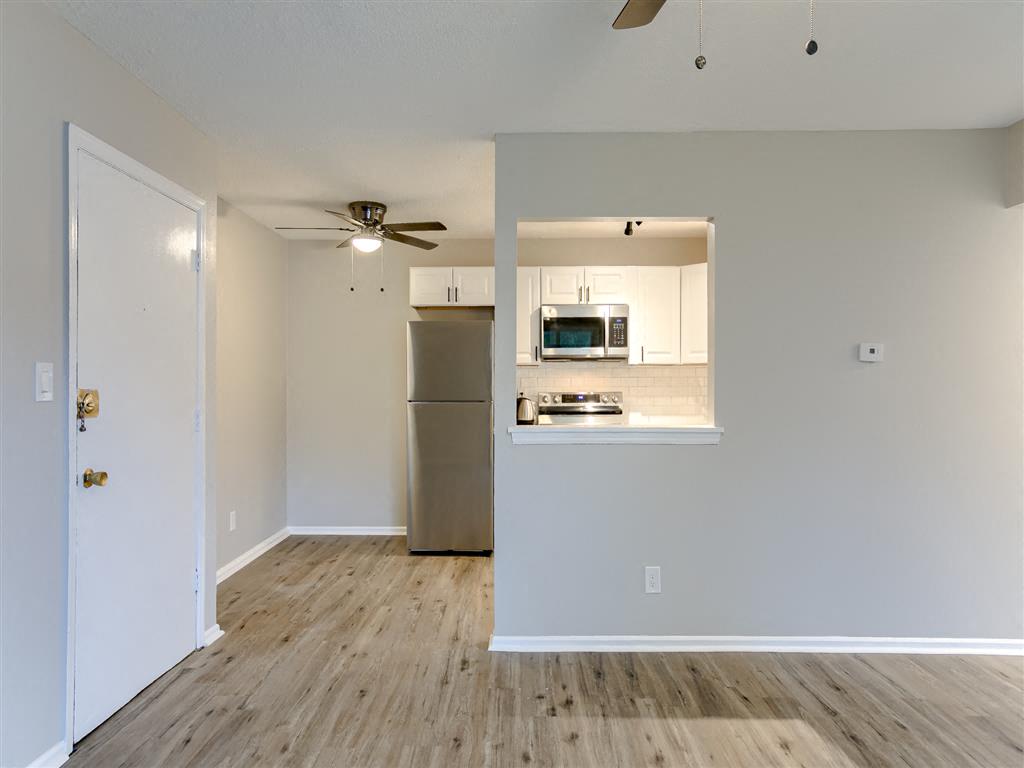an empty living room with a kitchen and a ceiling fan