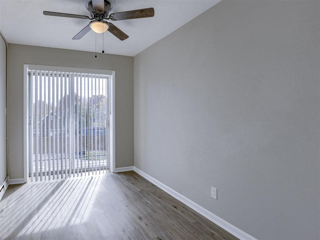 an empty living room with a large window and a ceiling fan