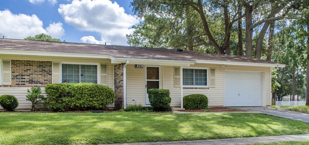 the front of a yellow house with a lawn and trees