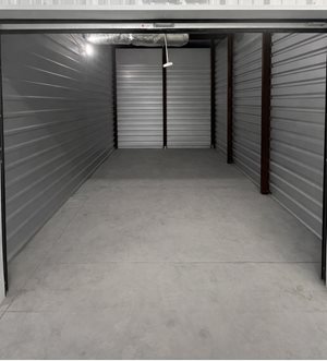 A spacious, empty storage unit with closed grey doors and a concrete floor.