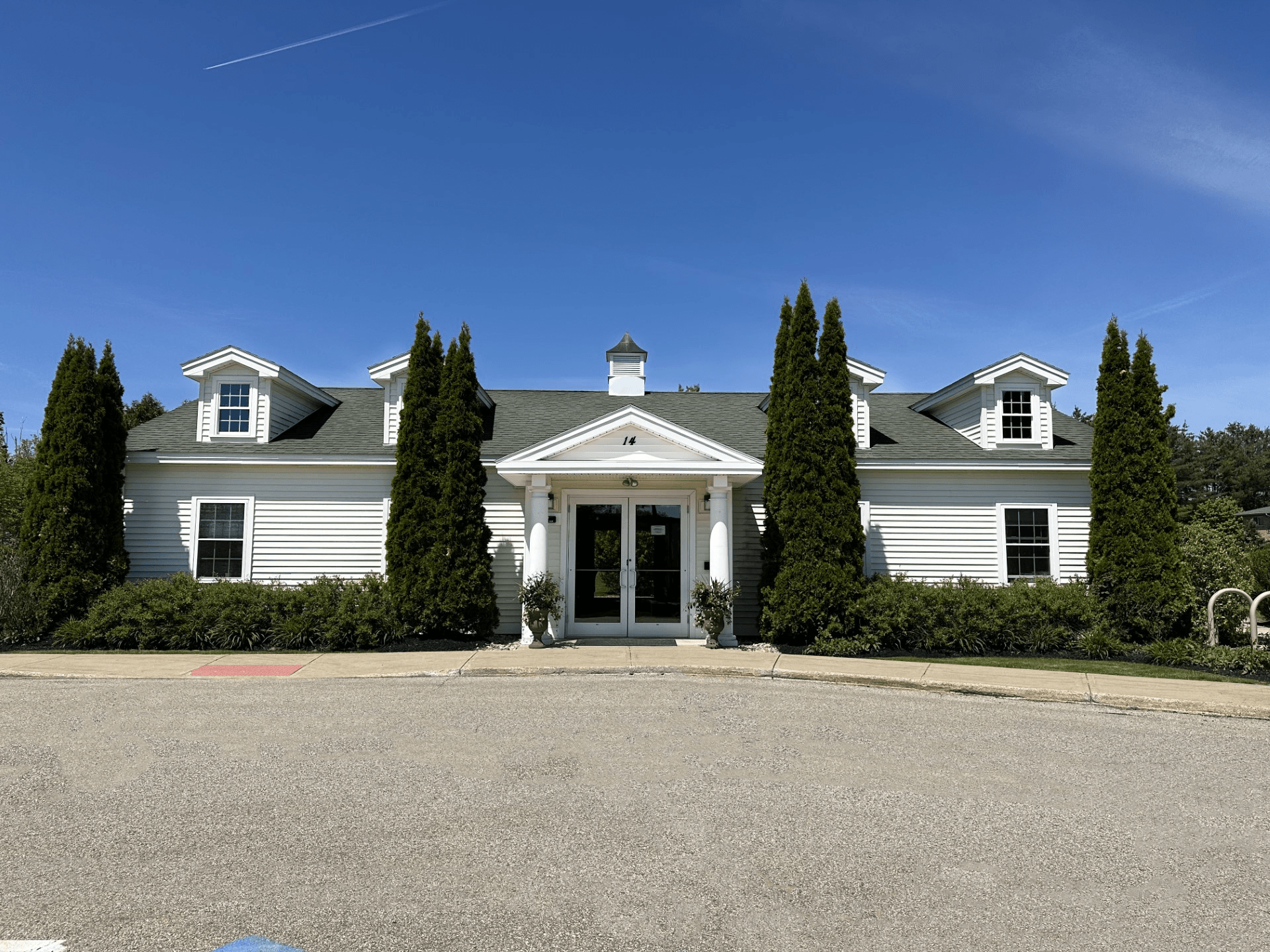 the front of a white house with trees and a blue sky