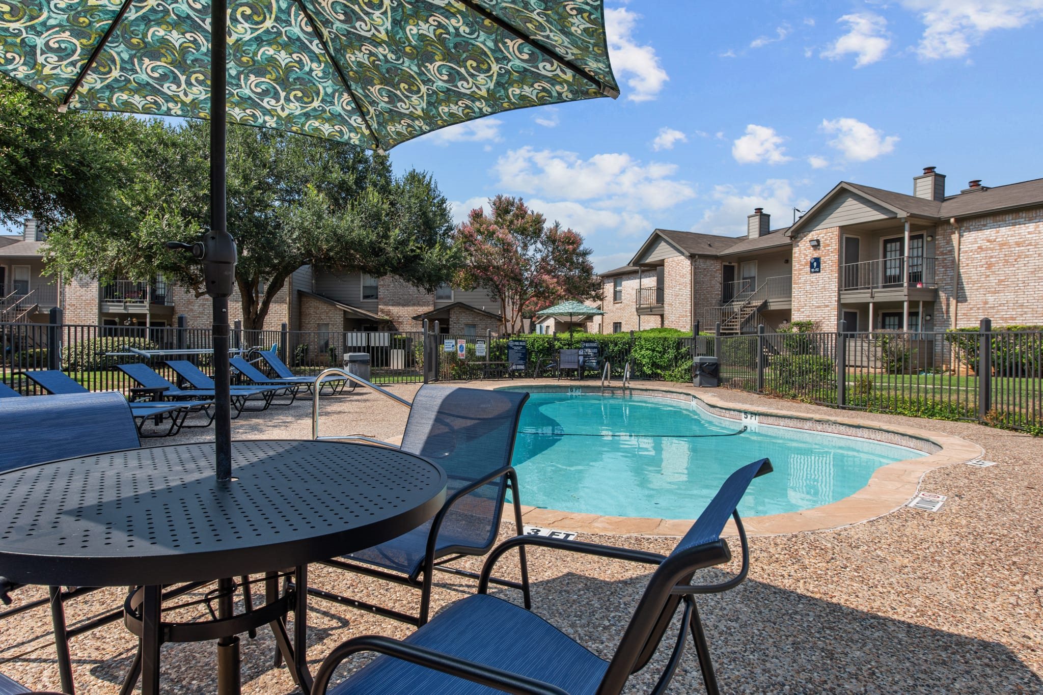 Pool area with patio furniture and decorative umbrella at Peaks at Universal City Apartments, Universal City, Texas