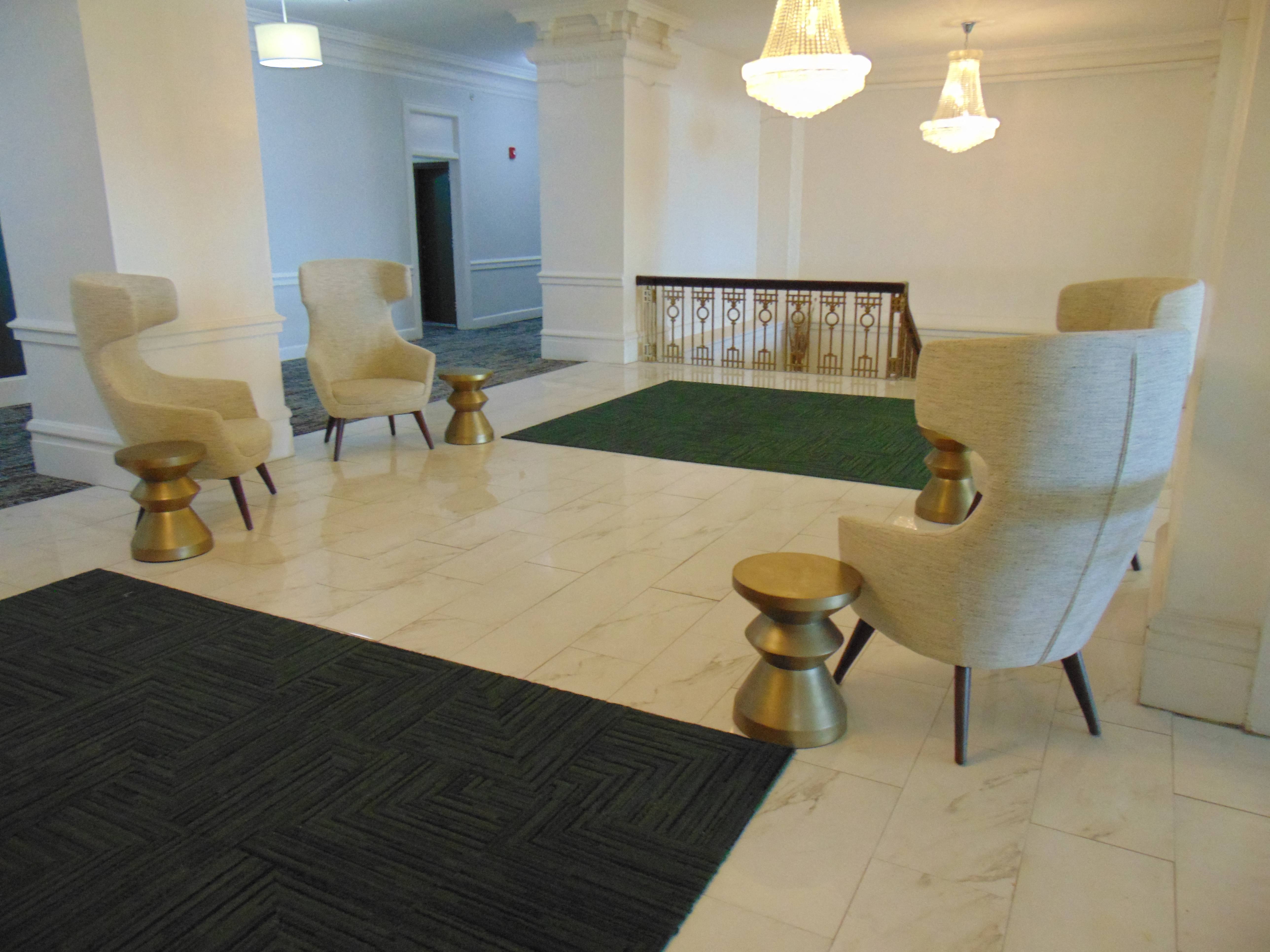 A room with a black and white patterned rug, a green rug, and four chairs.