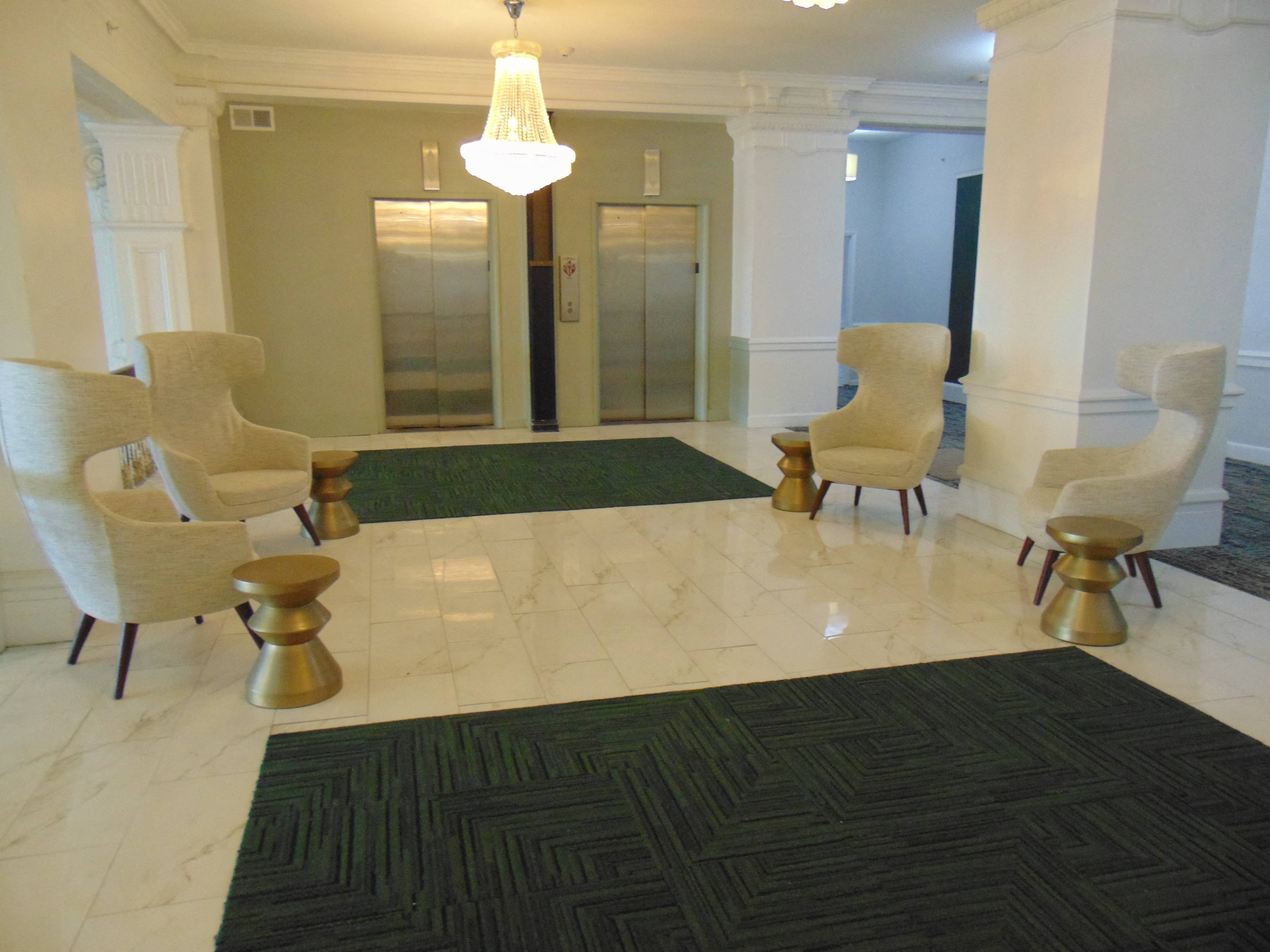 A hallway with chairs and a green rug.