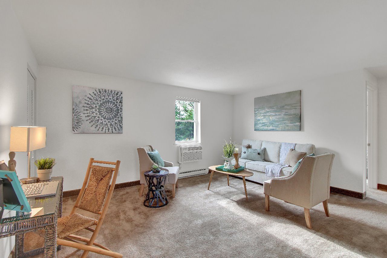 A living room with a white couch, a wooden chair, a glass table, and a painting on the wall.
