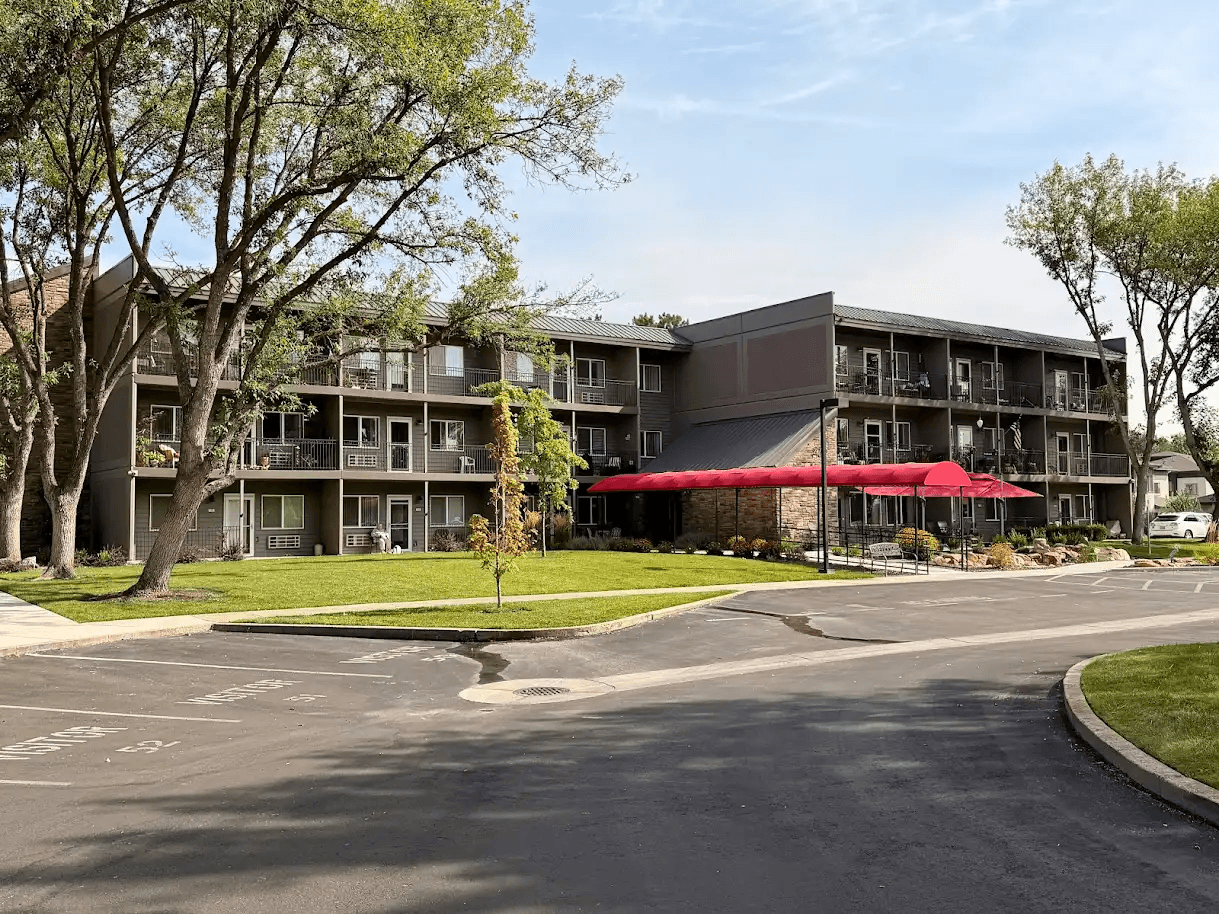 A large building with a red awning sits next to a tree-lined street.
