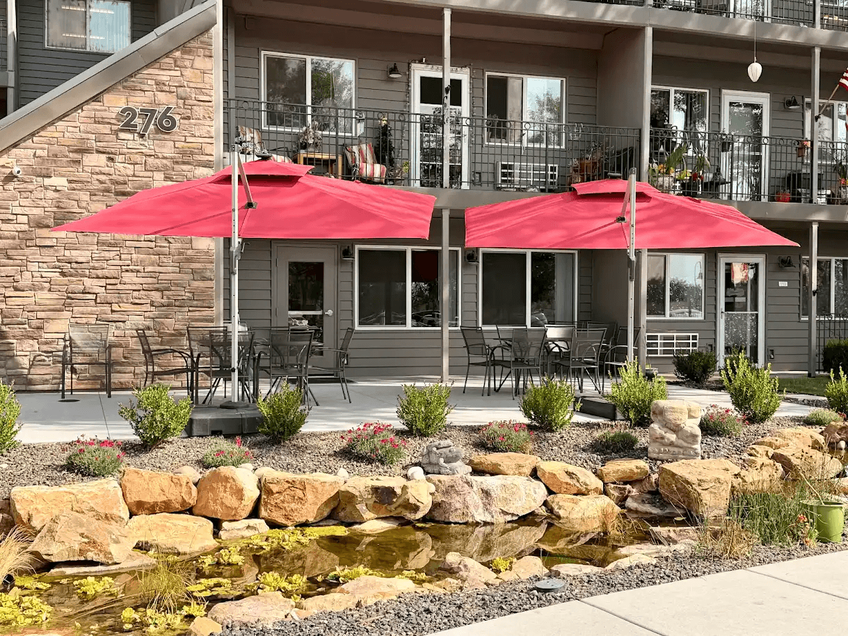 A patio with red umbrellas and a water feature in front of a building.
