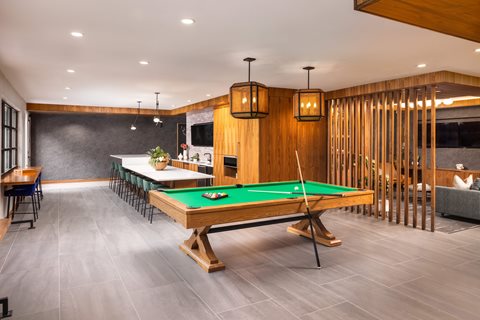 A pool table is in the middle of a room with a bar and a couch.