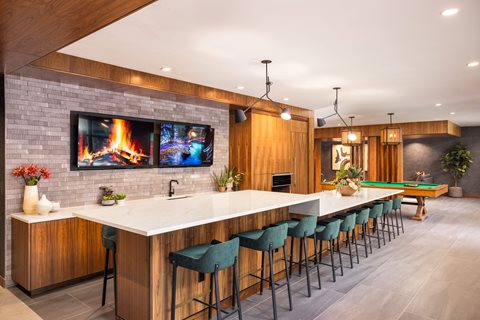 A modern kitchen with a bar area and a television displaying a fireplace.