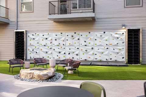 A white climbing wall with green and yellow holds is in front of a building.