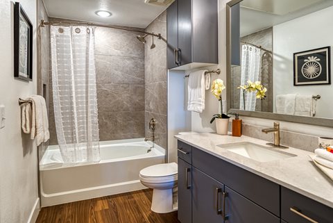a bathroom with gray cabinets and a white bathtub