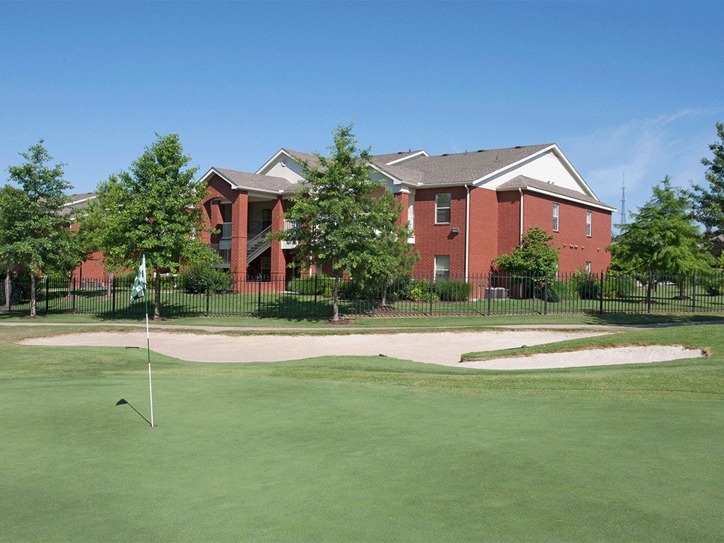 A golf course with a green lawn and a red building in the background.