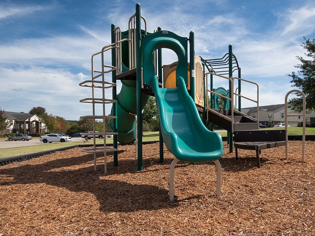 A playground with a green slide and a green bench.