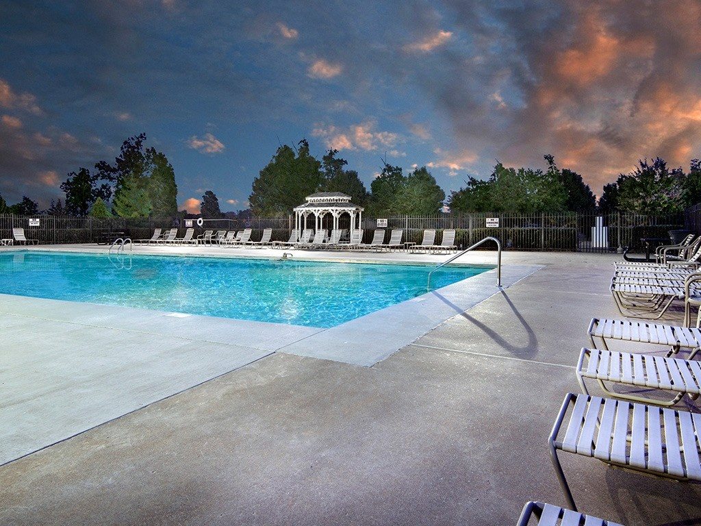 A pool with sun loungers and a pavilion in the background.