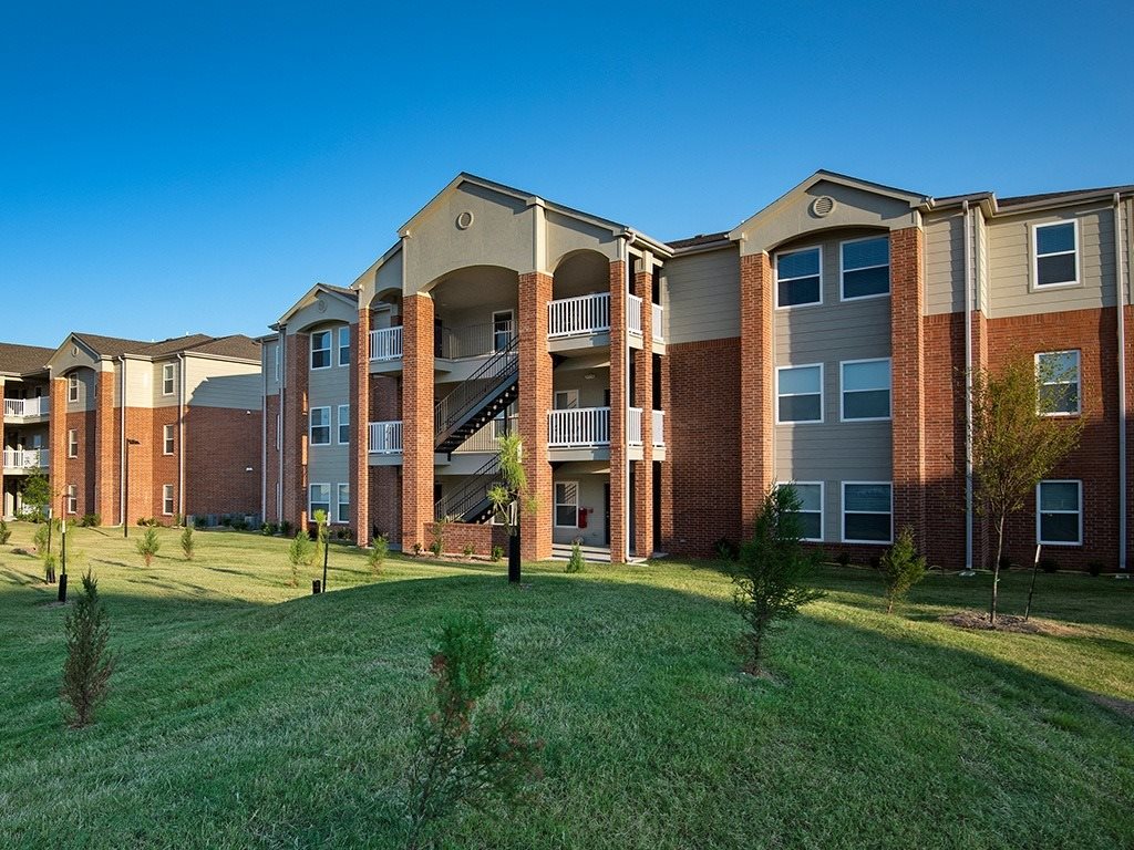 Apartment complex with red brick buildings and green grassy areas in front.