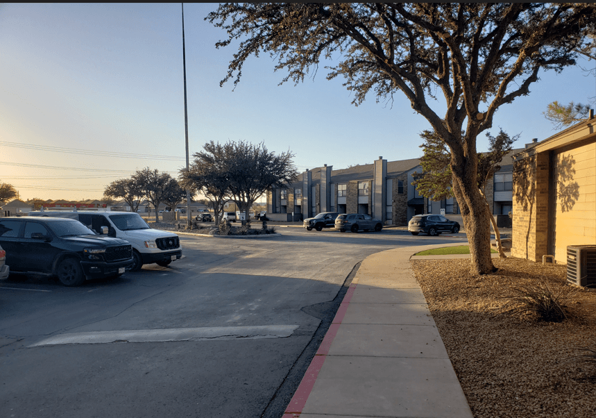Cars parked on the side of a street with a tree and a building in the background.