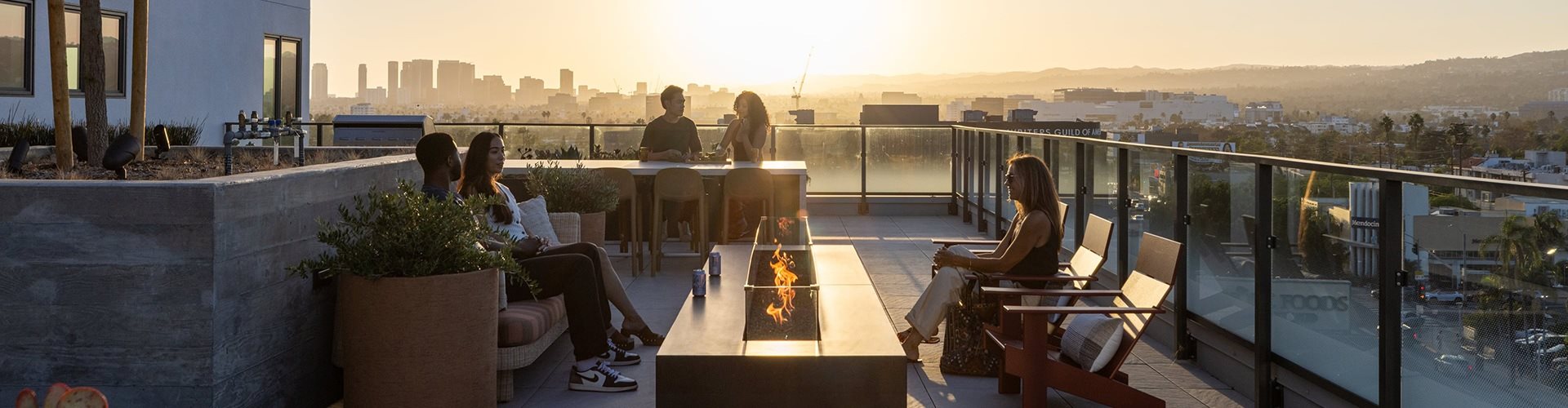 People are sitting on a balcony overlooking a city skyline at sunset.