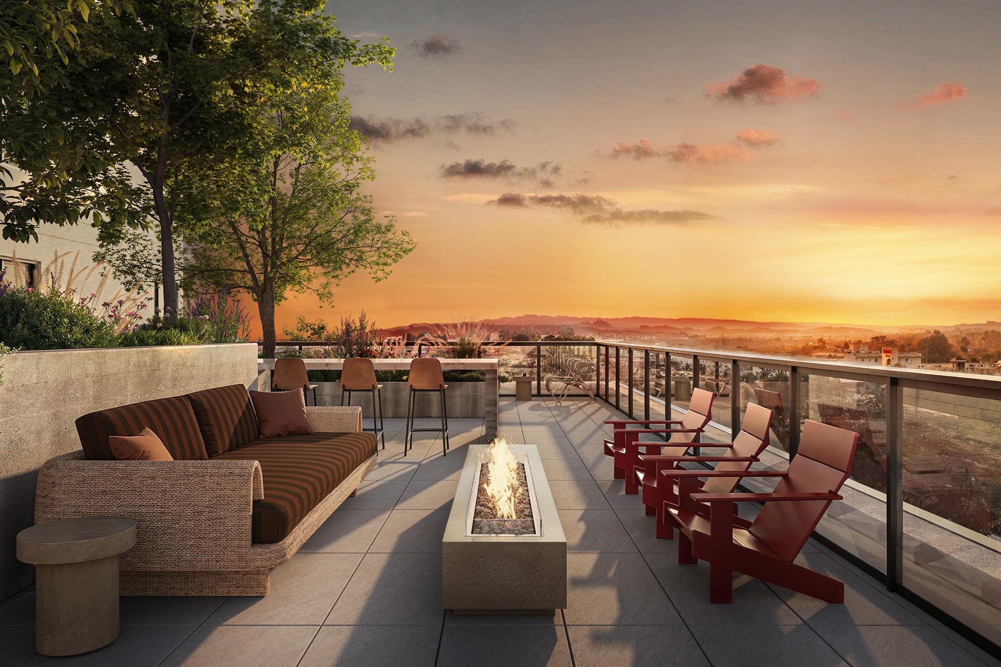 A patio with red chairs and a fire pit overlooks a sunset.