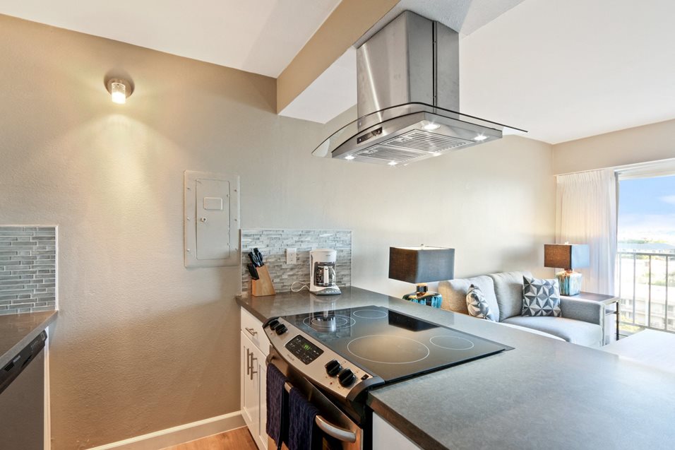 Kitchen with stainless steel electric range over range hood, gray quartz counters, wood-style floors
