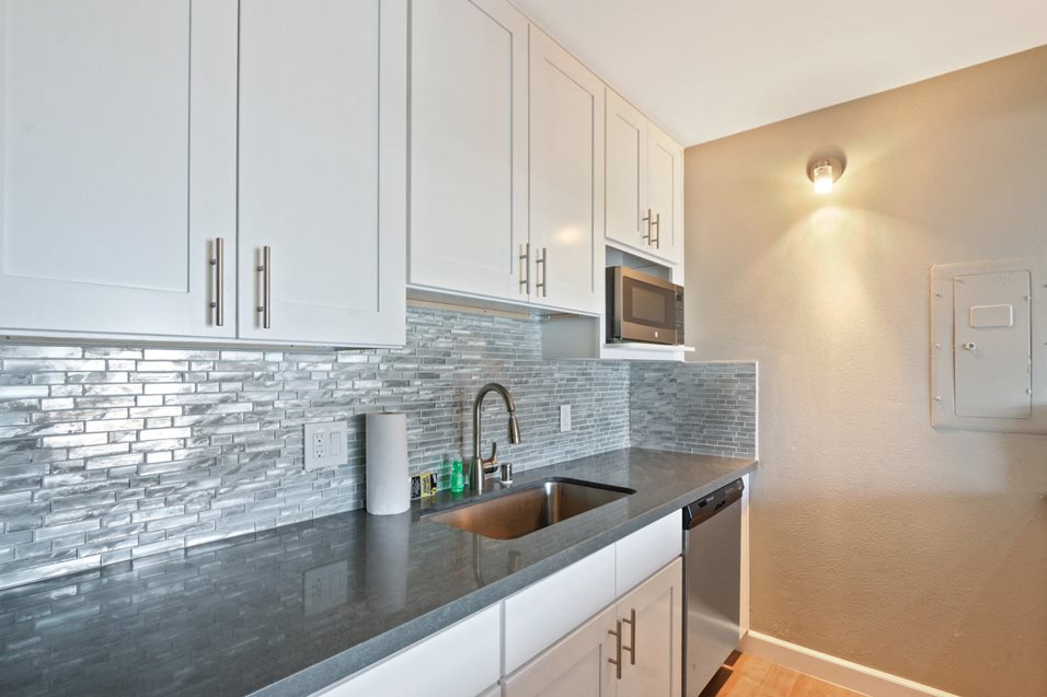 Kitchen with stainless steel dishwasher, microwave, single kitchen sink, white kitchen cabinets, tile backsplash