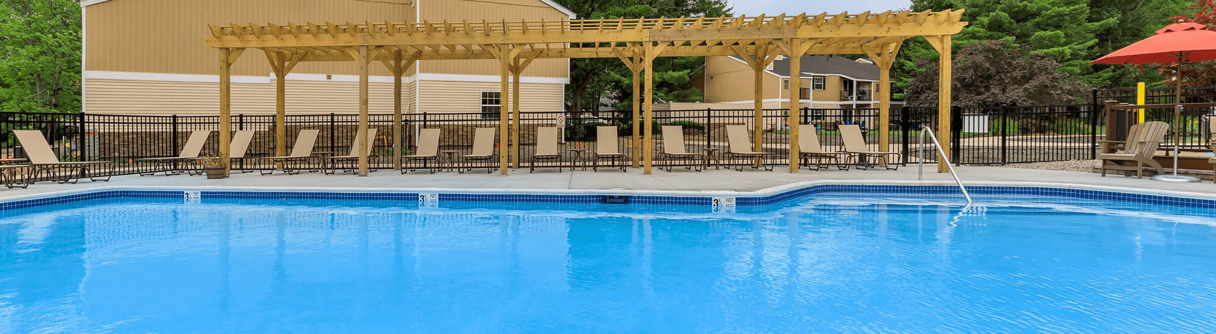 A large swimming pool with a wooden pergola over the seating area.