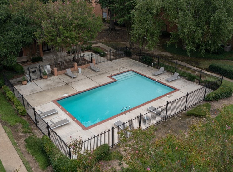 Fenced pool and sundeck surrounded by lush trees at Hampton House Apartments