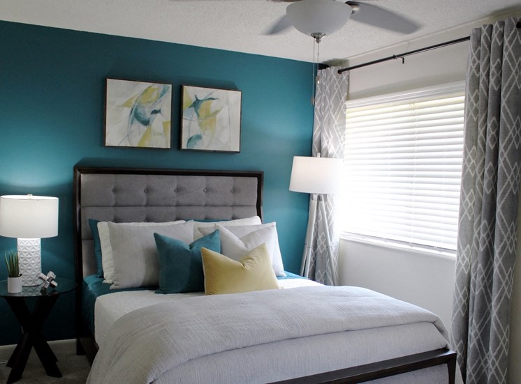 bedroom with large window, modern ceiling fan, teal accent wall and model furnishings
