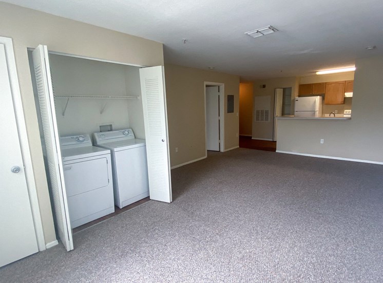Spacious living room with carpet flooring, full-sized washer and dryer connections, and kitchen breakfast bar