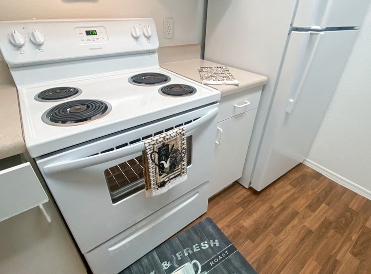 Kitchen featuring white cabinets, white appliances, tan countertop, and electric stove top with coils, wood style flooring, with floor mat and hand towels as décor